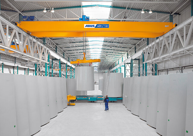 Laufkran in einer Industriehalle bewegt große Lasten, während ein Mitarbeiter im Arbeitsbereich steht.