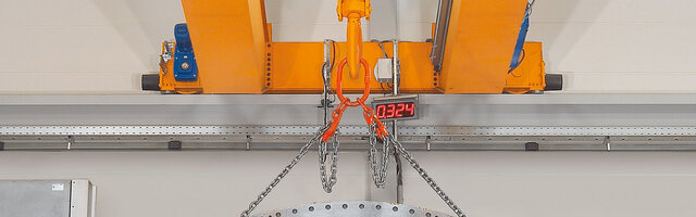 Fahrwerksträger mit Vorsatzstücken eines Krans, an dem ein Kettengehänge mit Last befestigt ist.