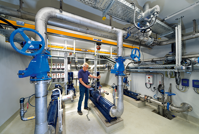 Mitarbeiter bedient ein Hängebahnsystem mit Kettenzug und bewegt eine Last in einer Werkhalle