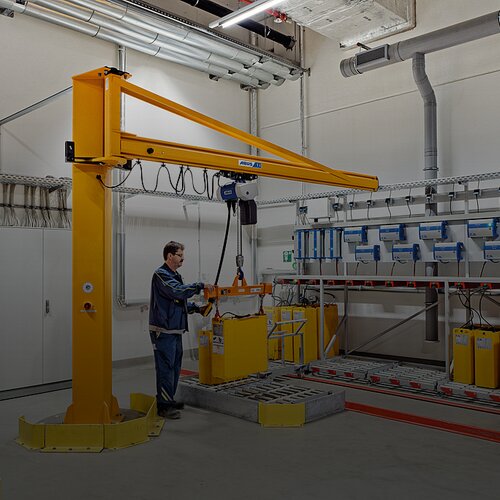 Mitarbeiter bedient einen Säulenschwenkkran und bewegt eine Last an einem Arbeitsplatz in einer Industriehalle