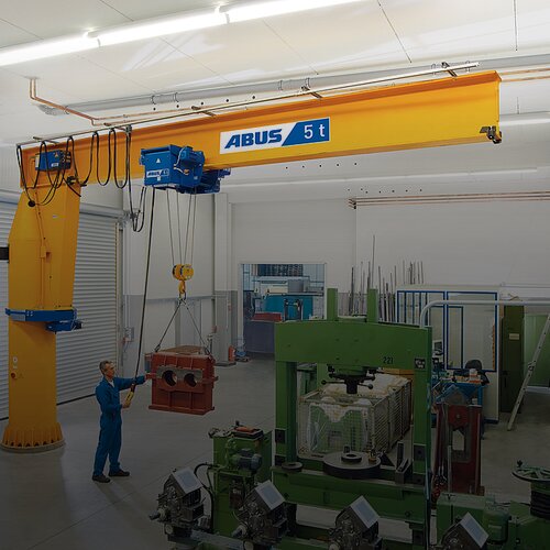 Mitarbeiter bedient einen Säulenschwenkkran und hebt eine große Last mit einem Kettenzug in einer Werkhalle