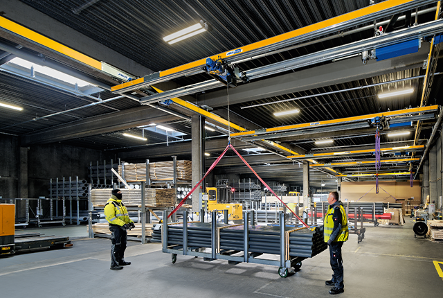 Zweiträgerkran ZHB hebt eine Last in einer Industriehalle, während Mitarbeiter den Vorgang begleiten.