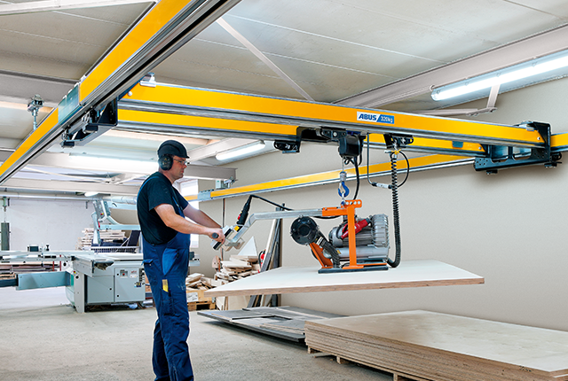 Mitarbeiter bedient einen Zweiträgerkran ZHB-X und hebt eine Last mit einem Kettenzug in einer Werkhalle.