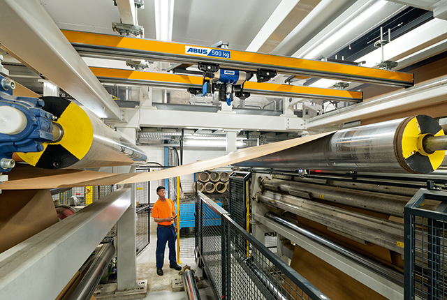 Zweischienenbahn transportiert Material entlang der Produktionsanlage, während ein Mitarbeiter den Prozess begleitet.