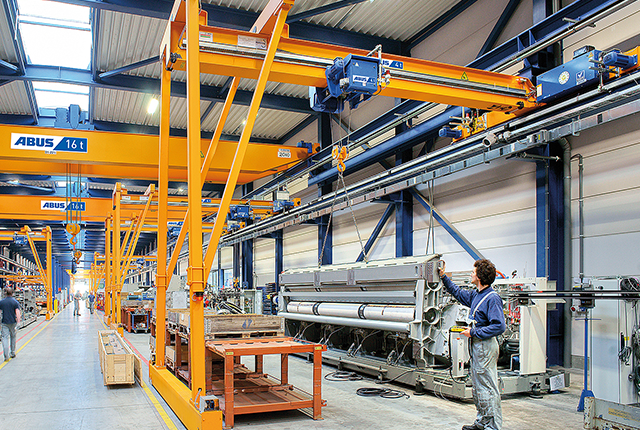 ABUS Halbportalkran in einer Industriehalle mit Tragfähigkeit bis 10 t und Spannweite bis 15 m für flexible Materialbewegung an Arbeitsplätzen.
