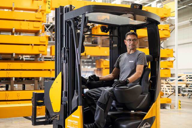 Mitarbeiter sitzt in einem Gabelstapler und transportiert ein Werkstück durch eine Industriehalle